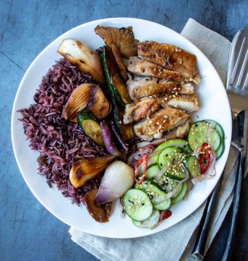 Grilled chicken, rice, and cucumber salad on a white plate