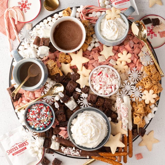 A large round hot chocolate charcuterie board with Swiss miss hot chocolate , whipped cream, and dippers