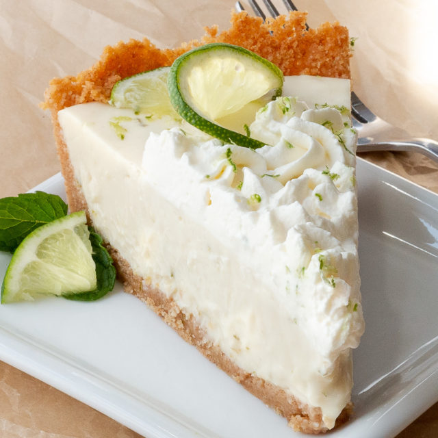 A slice of key lime pie with whipped cream and a fresh slice of lime.
